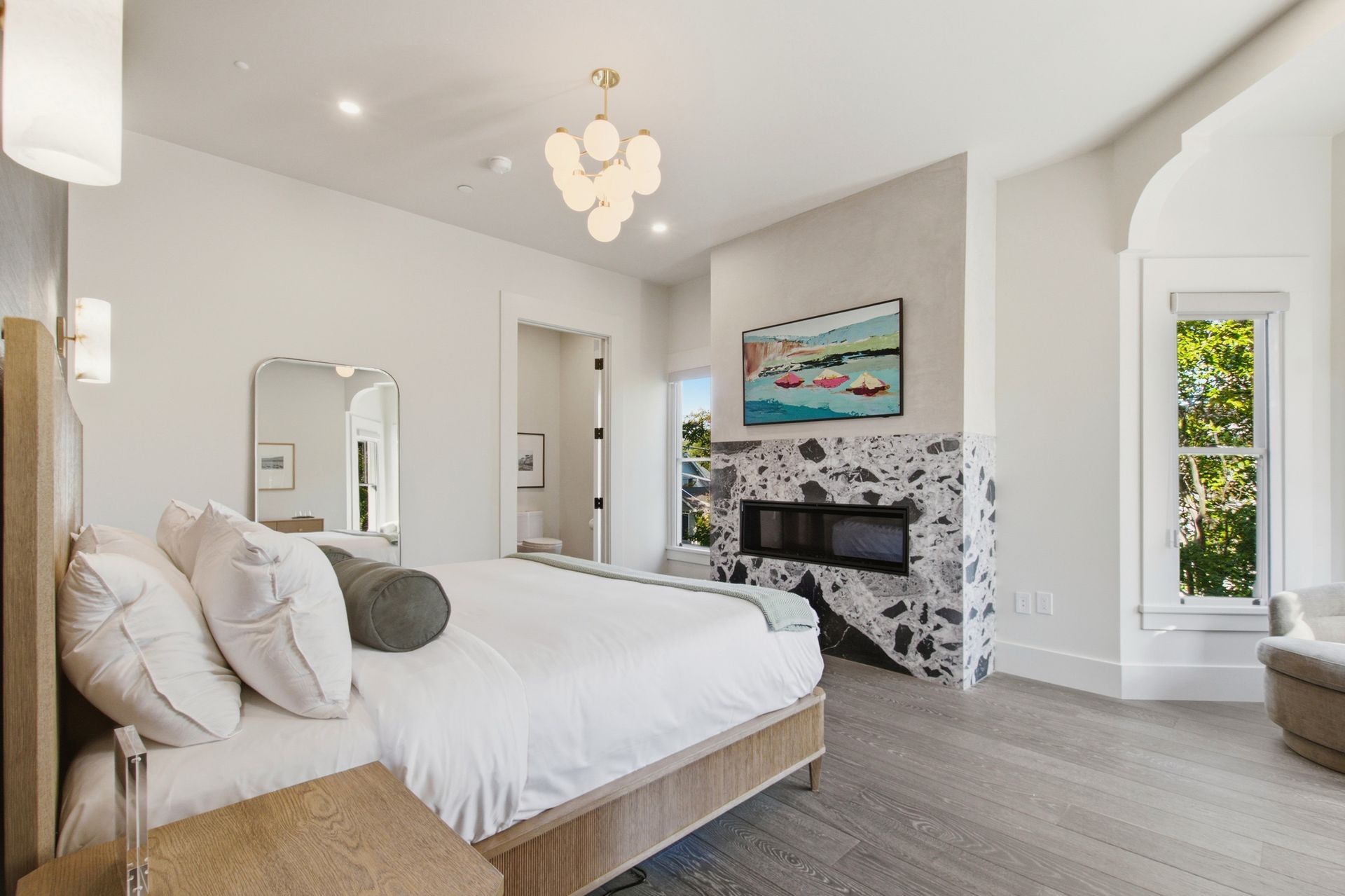 Bright airy bedroom with a white bed, floral accent wall, fireplace, and large window.