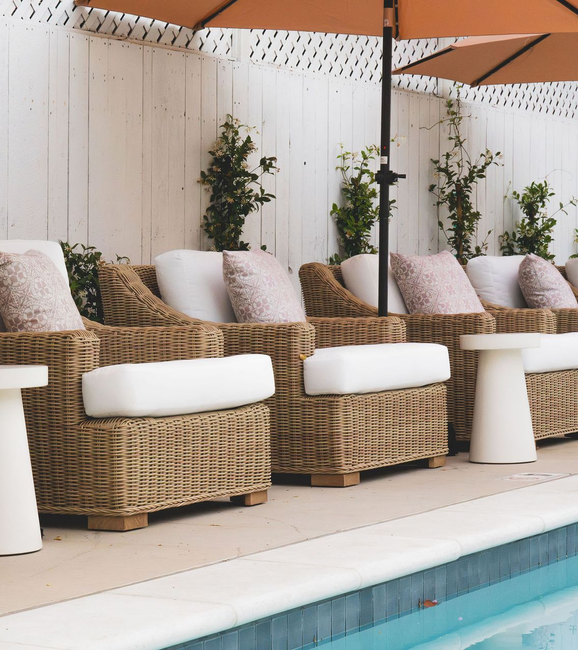 Poolside wicker lounge chairs with white cushions under beige umbrellas on a patio