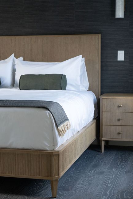 Modern bedroom with a neatly made bed, gray walls, and a wooden nightstand