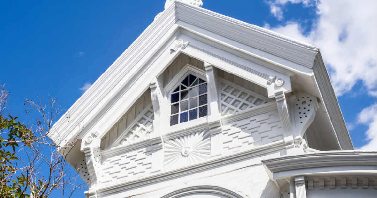 White Victorian house facade with ornate trim and a peaked roof against a blue sky
