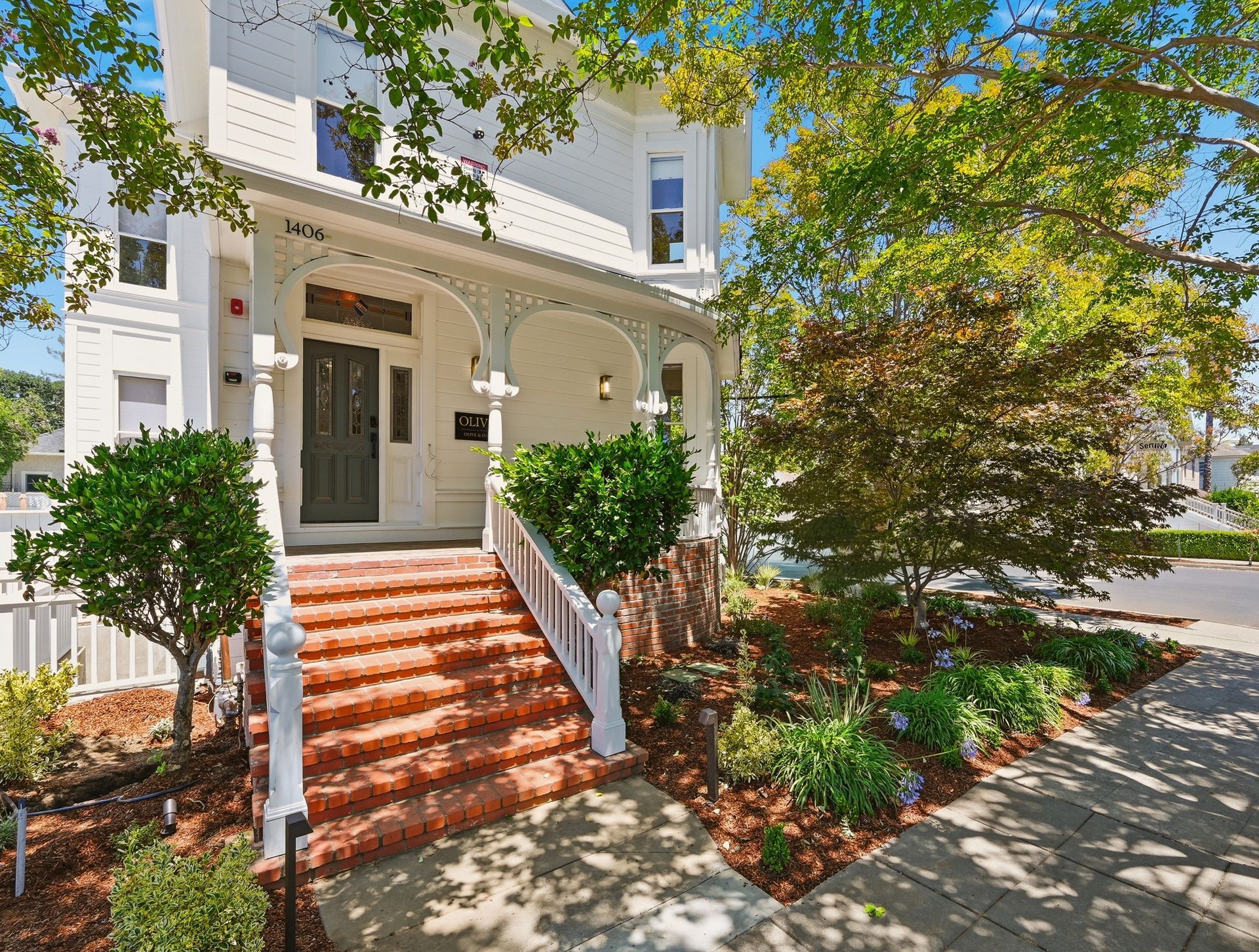 Aerial view of a white house with gray roof, front porch, and fenced yard on a residential street