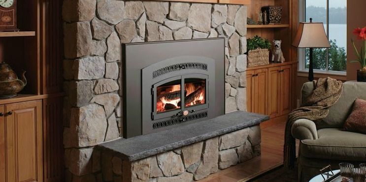 A fireplace with a stone surround, bench, and burning fire, beside a wooden cabinet and couch in a home.