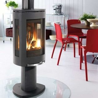 Modern fireplace with flames, in a brightly lit room with red chairs and a round table.