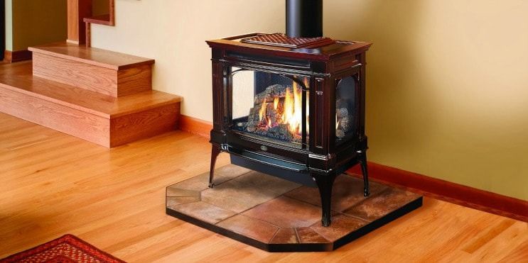 A lit fireplace stove on a tiled hearth, next to wooden stairs and a wooden floor.