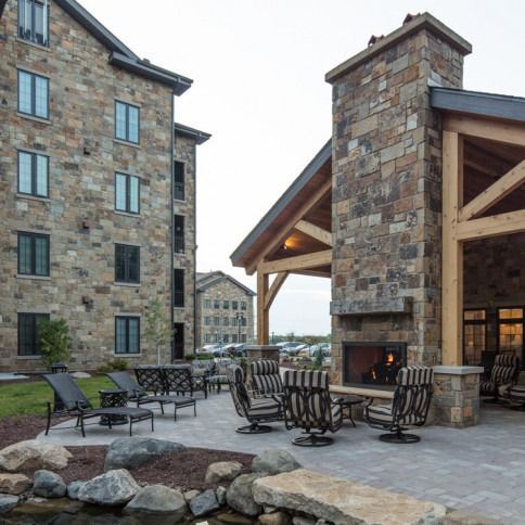 Outdoor patio with stone fireplace, seating, and multi-story stone building.