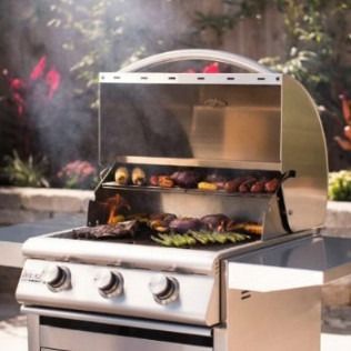 Stainless steel grill with open lid, grilling various foods; smoky outdoor setting.