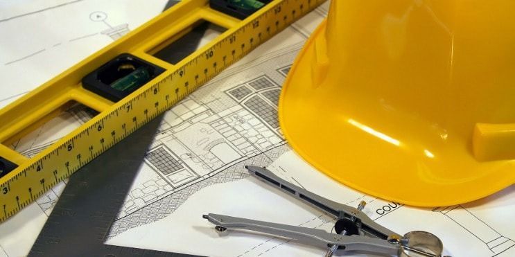 Construction tools, including a level, hard hat, and compass, sit on a blueprint.