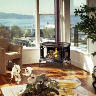 Cozy living room with a lit fireplace, armchair, and large windows overlooking a waterfront view.