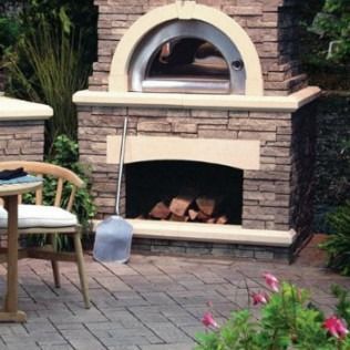 Outdoor stone pizza oven with wood, shovel, and patio furniture.