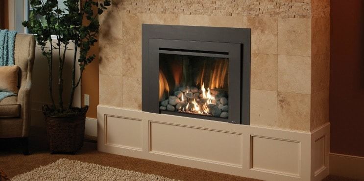 Fireplace with burning flames, set in a stone wall with a white panelled base. A potted plant sits to the left.