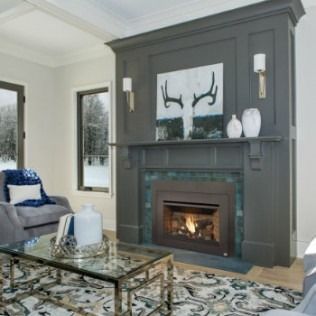 Dark gray fireplace with artwork, sconces, and decor in a modern living room with a rug and glass coffee table.