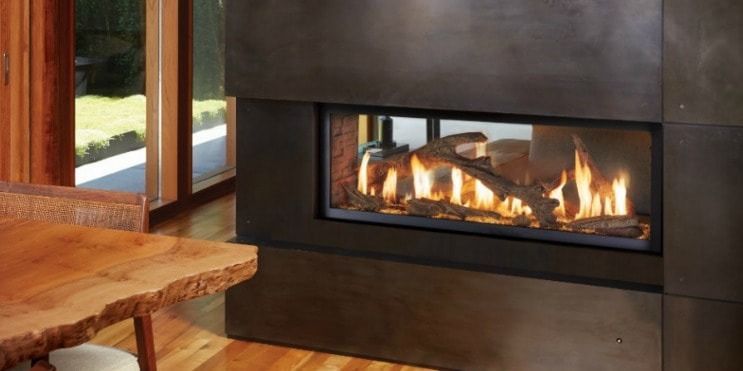 Modern fireplace with flames, inside a dark gray surround, with wooden table in the foreground.
