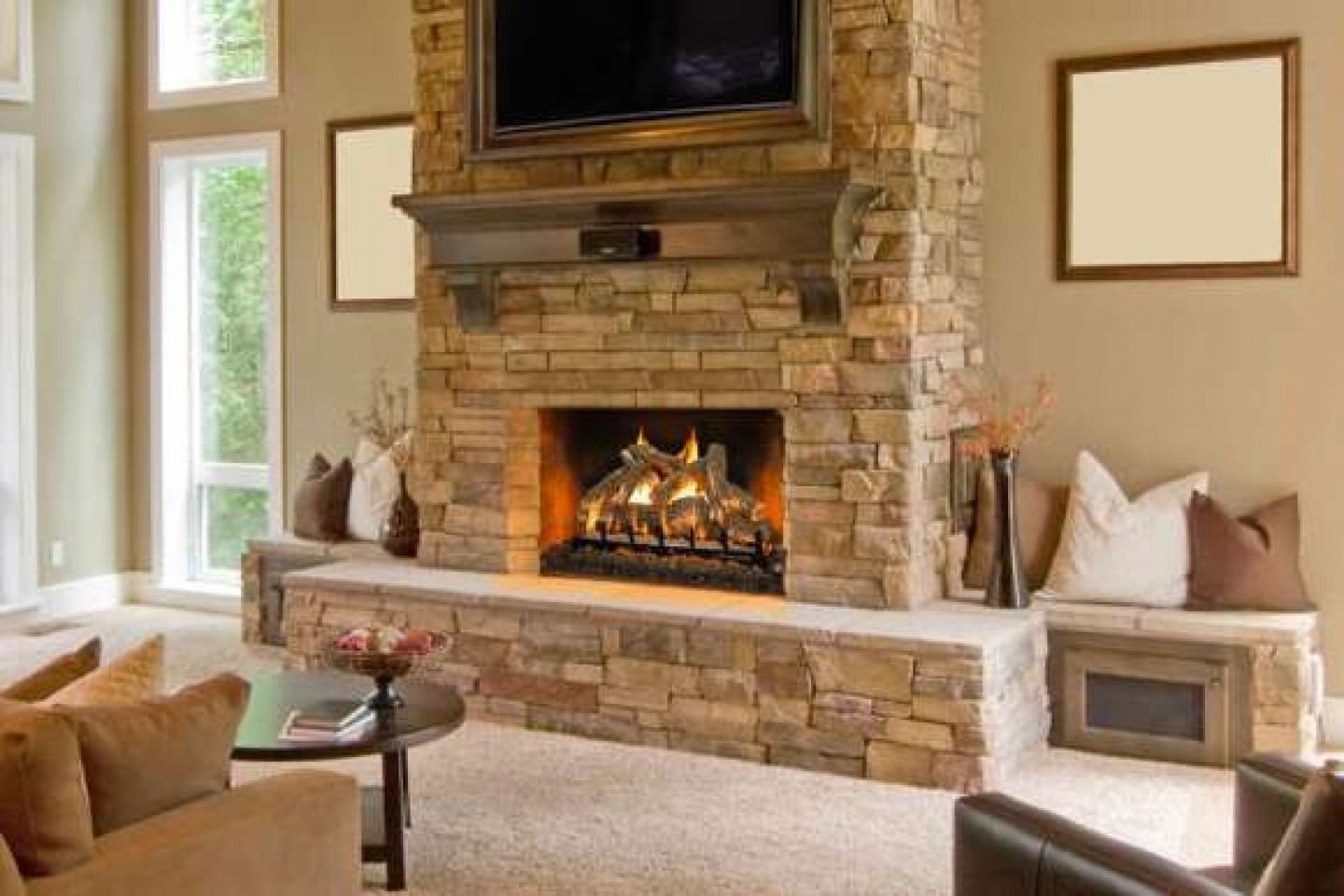 Stone fireplace with TV above, flanked by windows and framed artwork, pillows on benches.