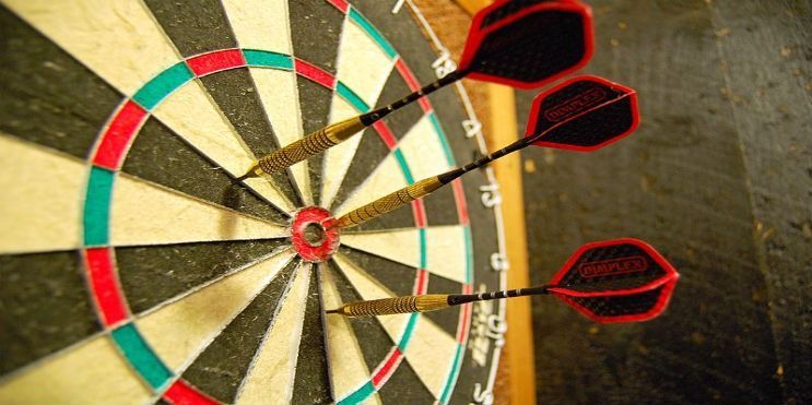 Three darts hit the bullseye on a dartboard, red and green rings surround the center.