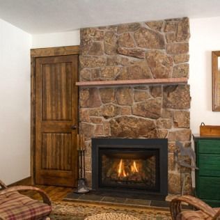 Stone fireplace with a burning fire, next to a wood door and green cabinet.