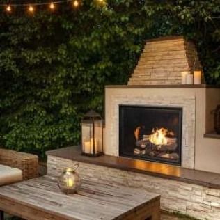 Outdoor fireplace with a stone chimney, fire burning, with a wooden table and candle lantern.