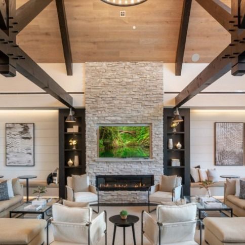 Living room with stone fireplace, wood beams, built-in shelving, and neutral-toned furniture.