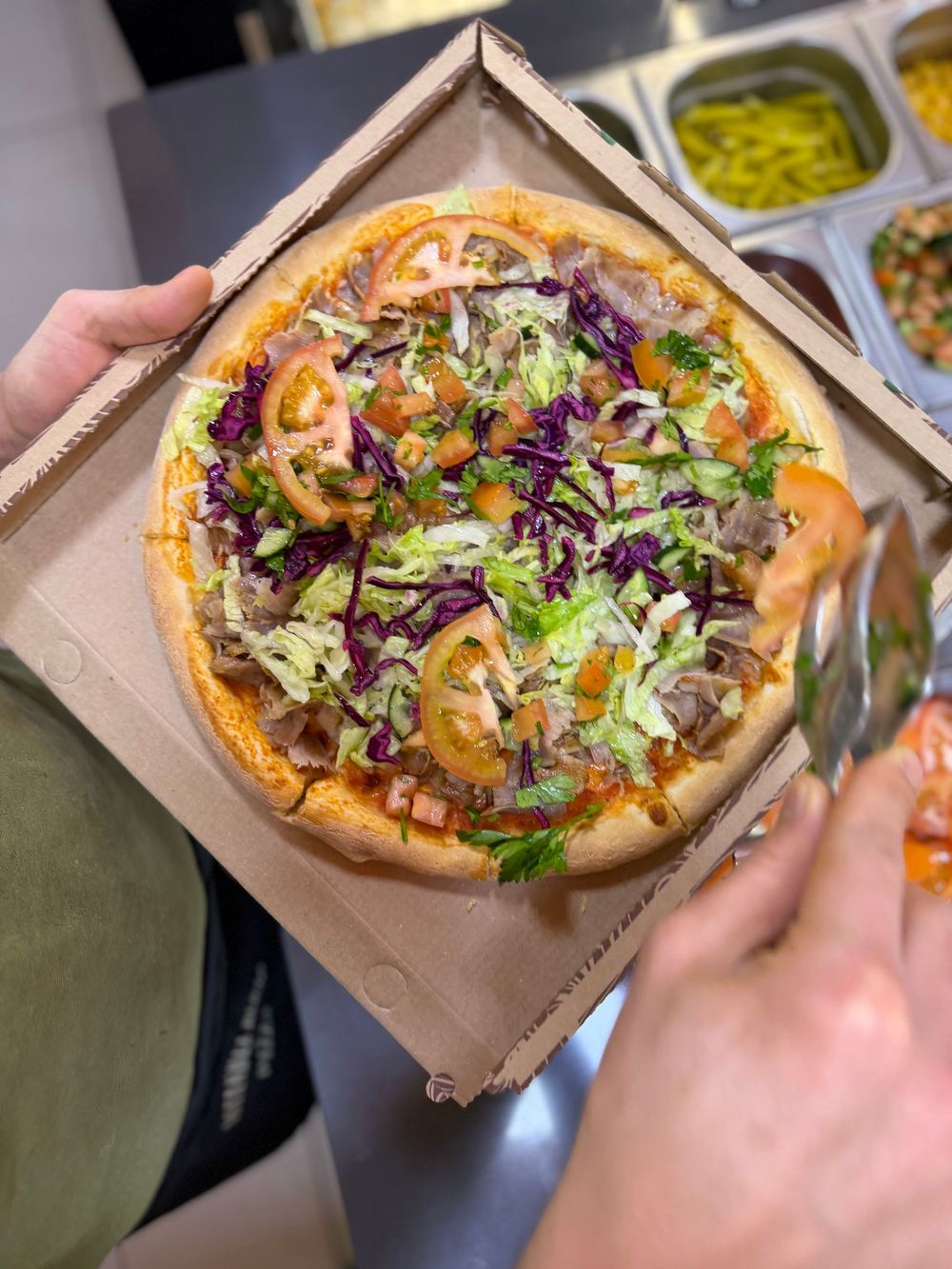 Una pizza rotonda condita con salsiccia a fette, olive nere, peperoni verdi e formaggio fuso, adagiata su un piano di lavoro maculato.