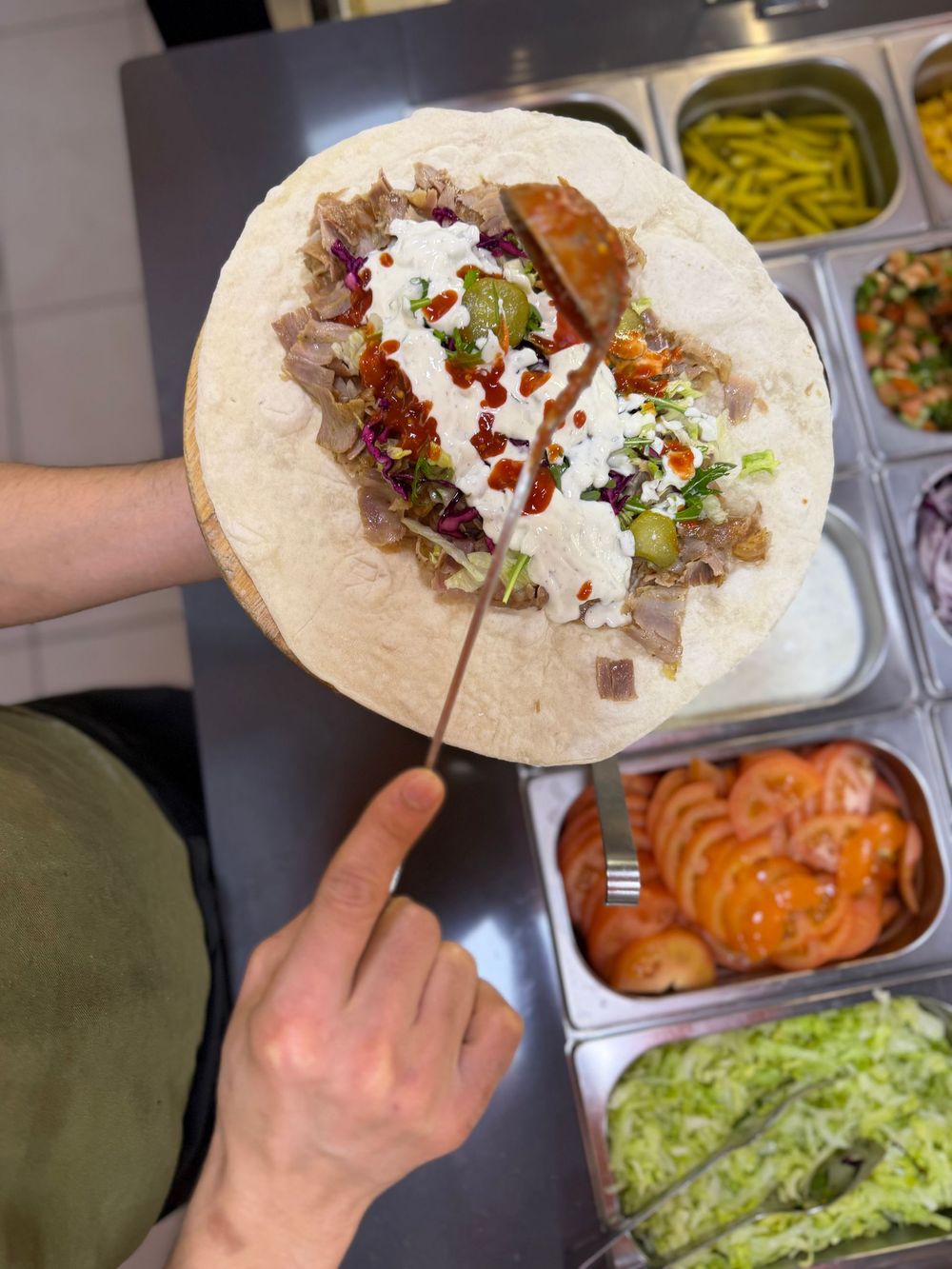 Otto piatti di shawarma, guarniti con patatine fritte, insalata e salsa bianca cremosa, disposti su un bancone della cucina.