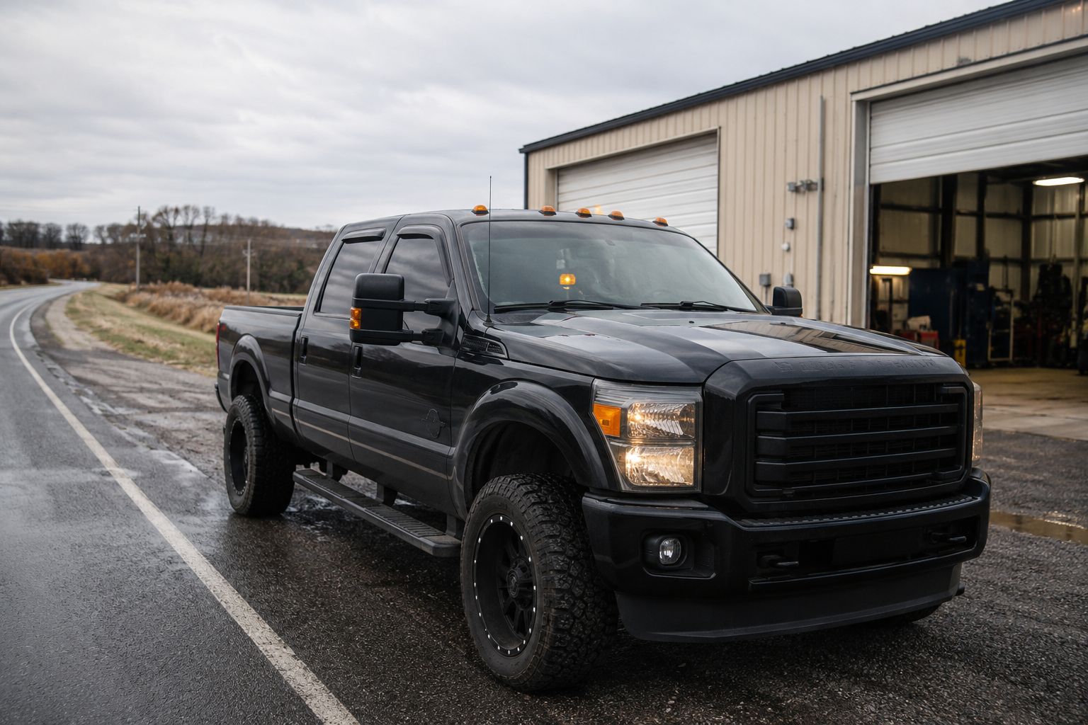 Black pickup truck parked outside a garage on a wet roadside.