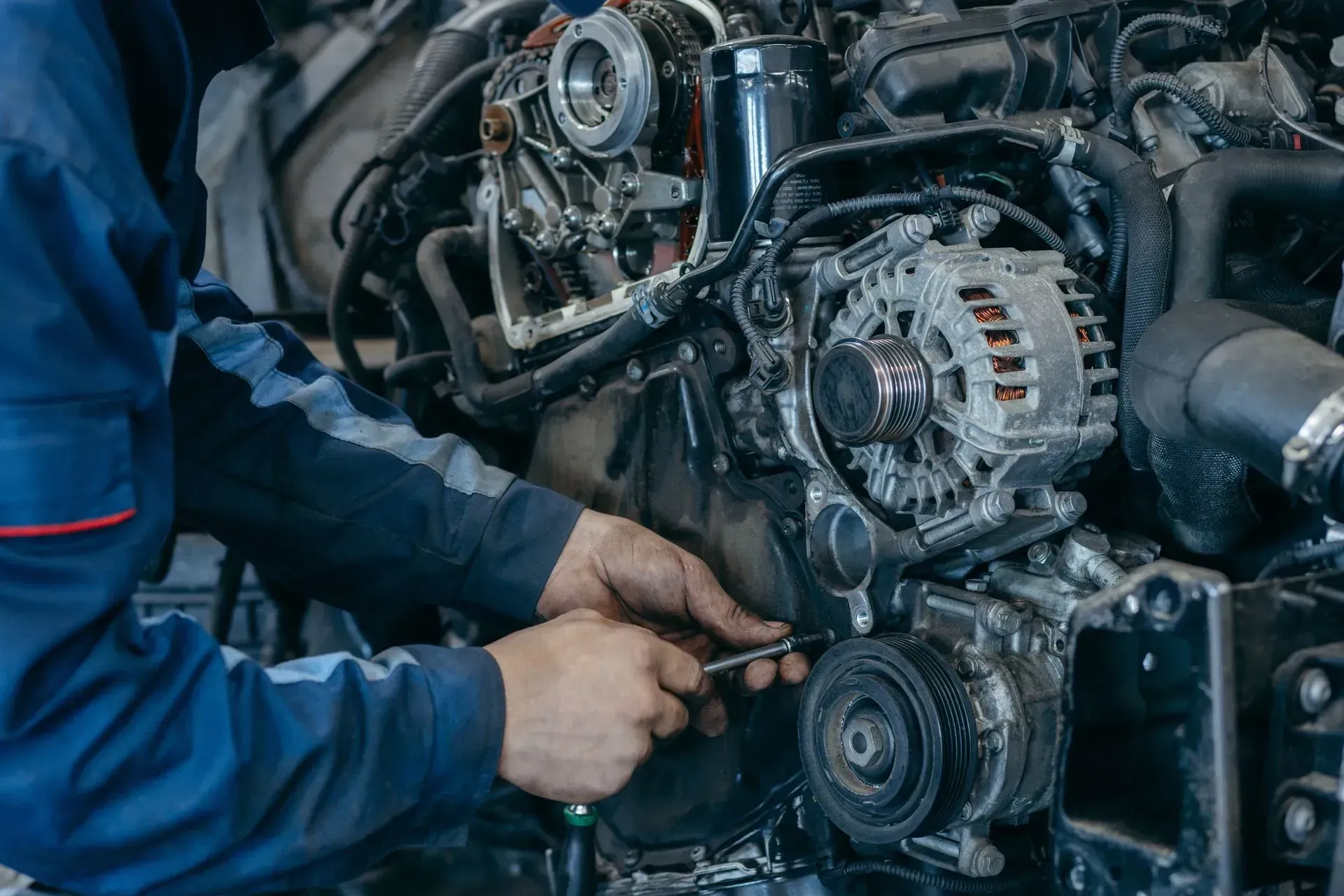 Mechanic in blue overalls repairing a car engine with a wrench in a garage