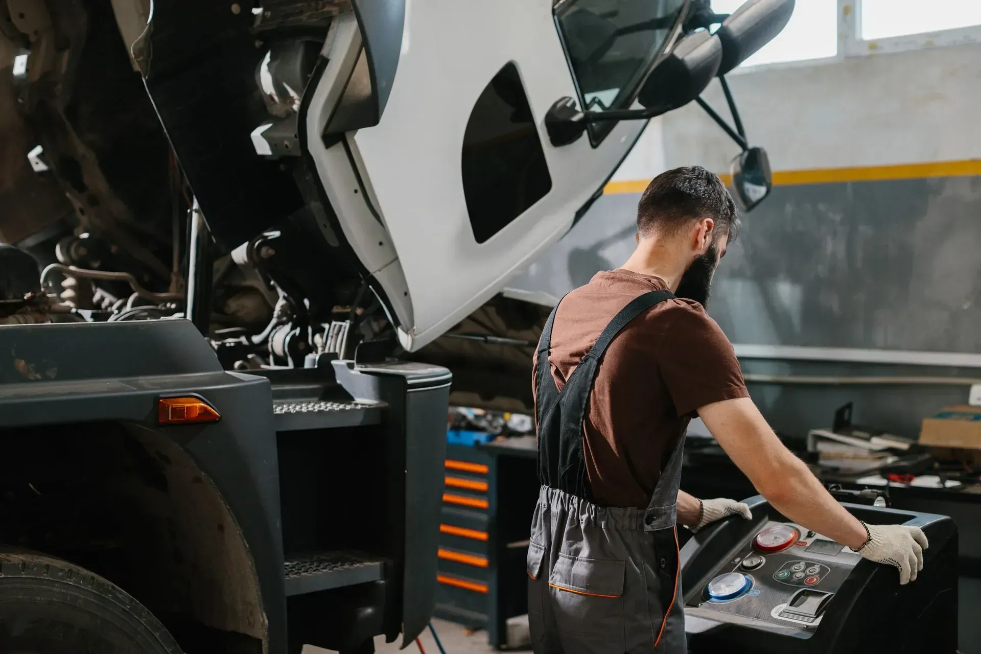 Mechanic working on a truck in a garage, with the vehicle hood open and tools on a workbench.