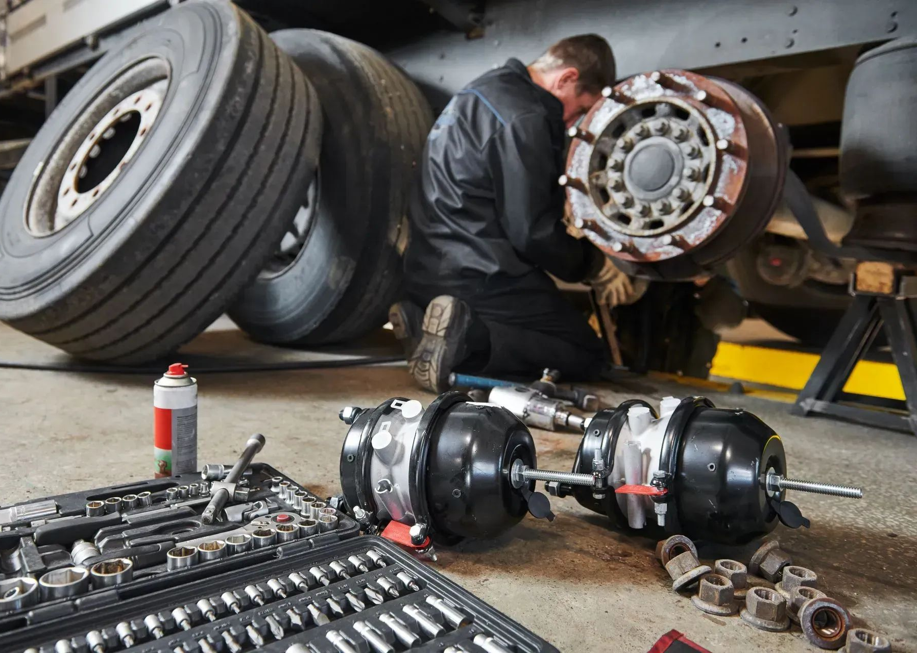 Mechanic repairing a truck axle beside tires and tools in a garage