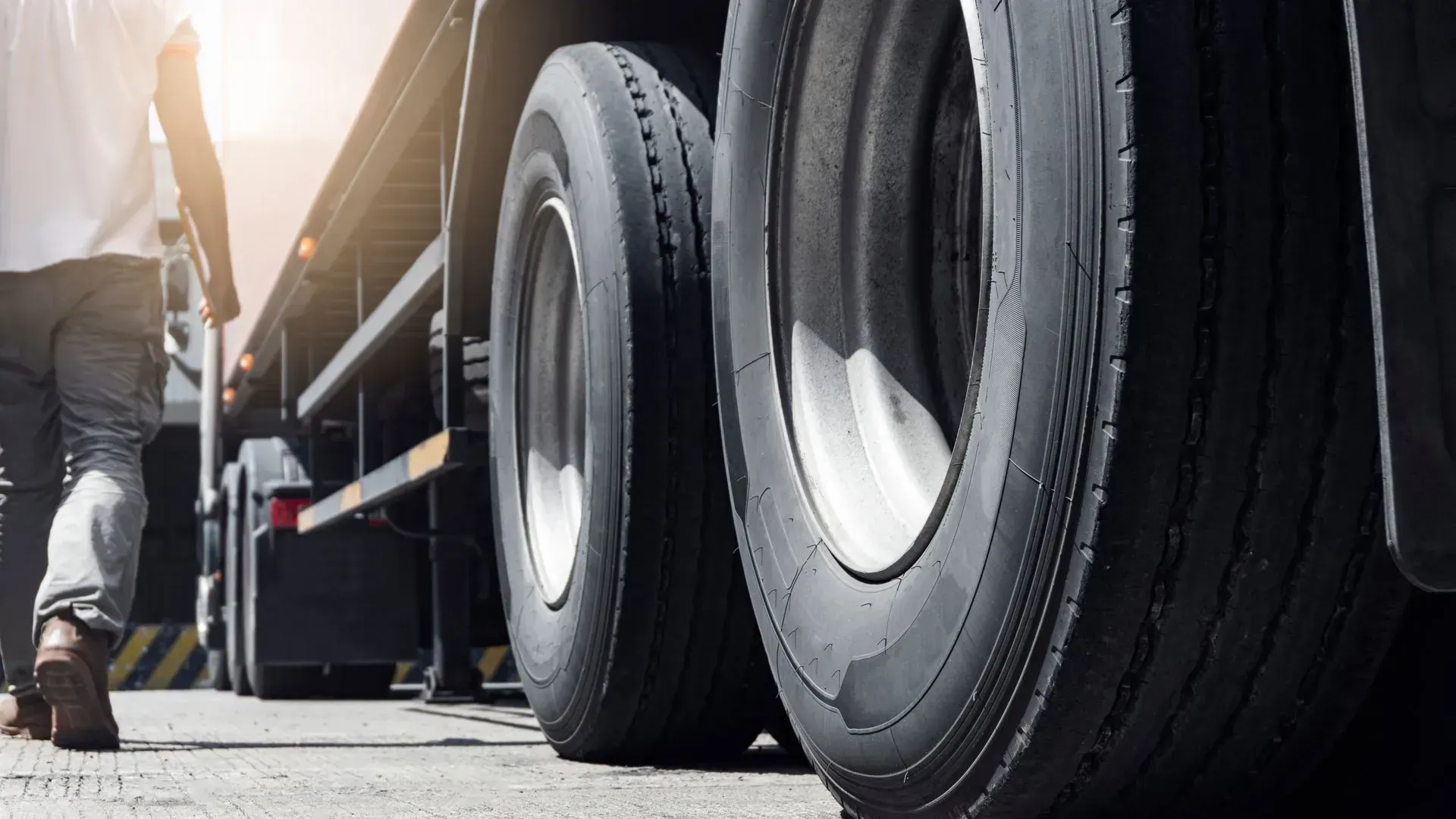 Person walking beside a truck with large black tires on a sunny street