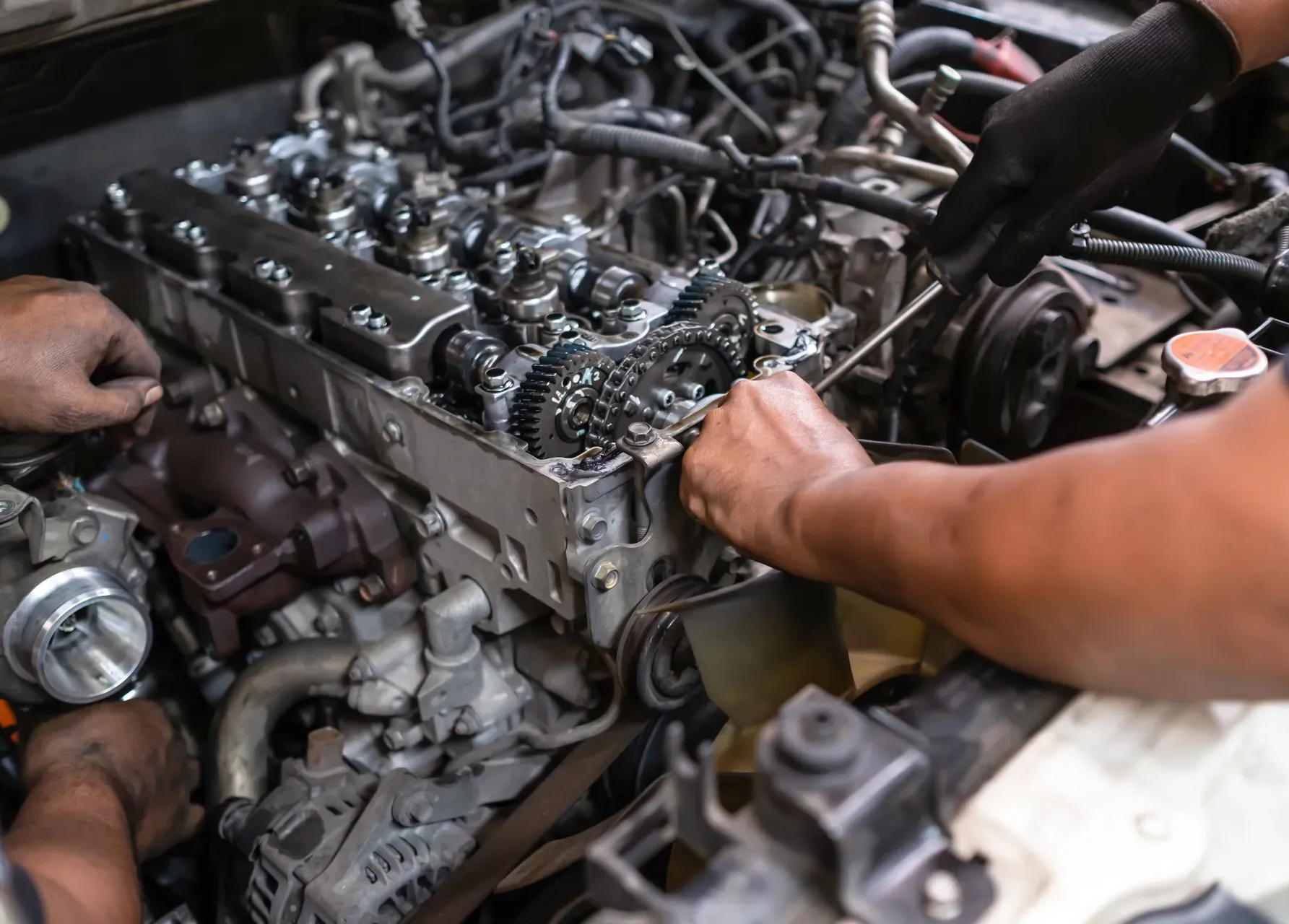 Mechanic working on a car engine with exposed gears and hands using tools in a garage