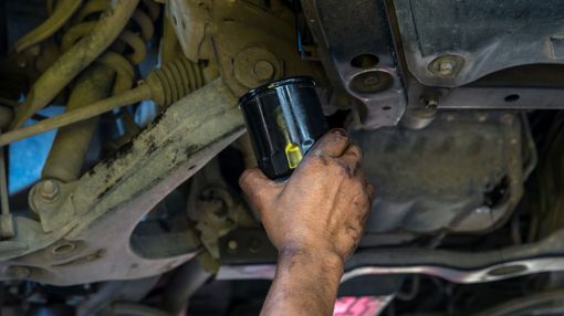Mechanic’s hand holding a black oil filter under a vehicle during an oil change