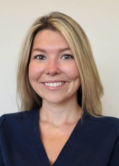 A person with blonde hair and a friendly smile, wearing a dark blue top against a plain white background.