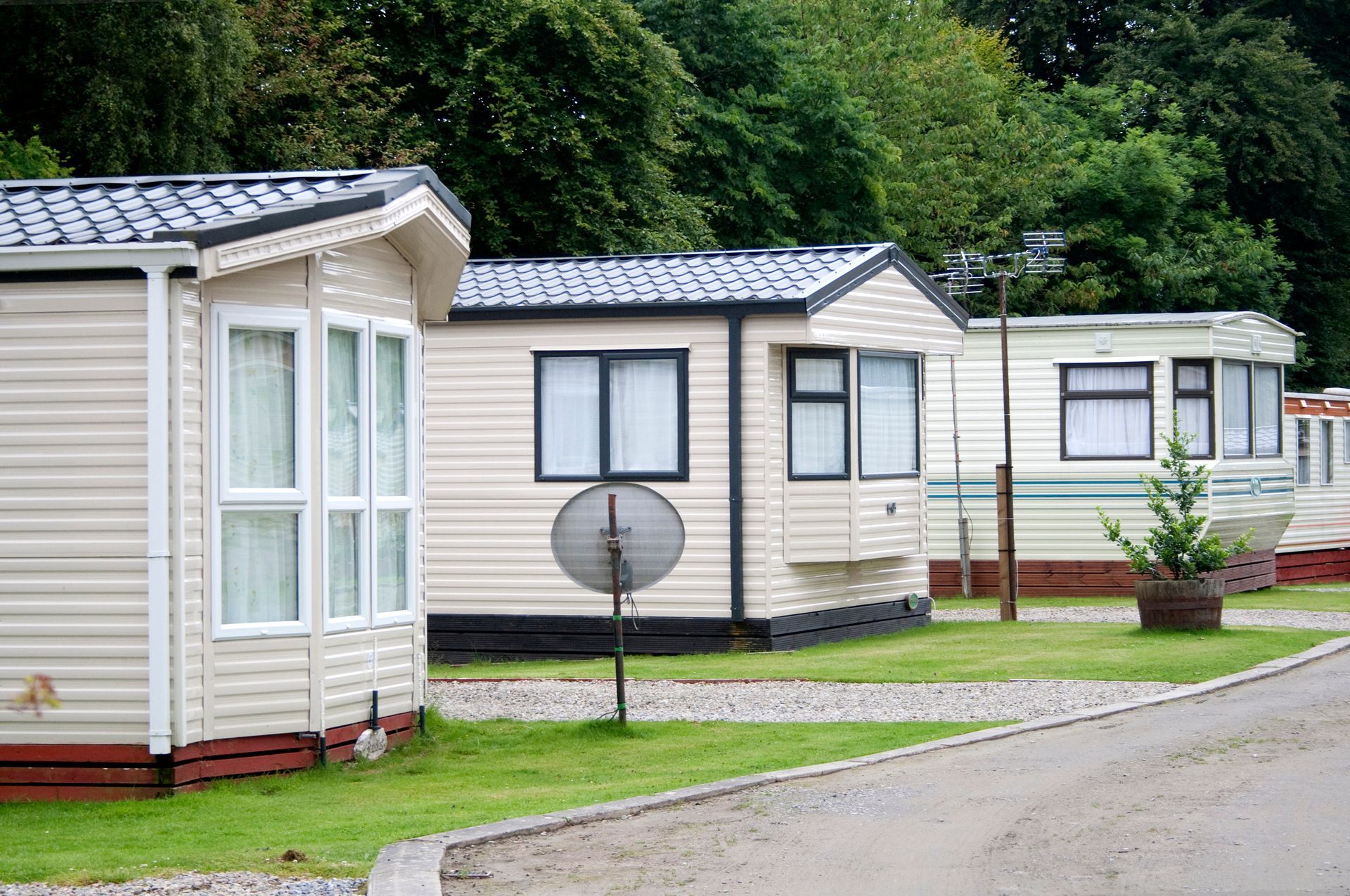 Row of modern cream mobile homes on a green lawn in a peaceful holiday park setting.