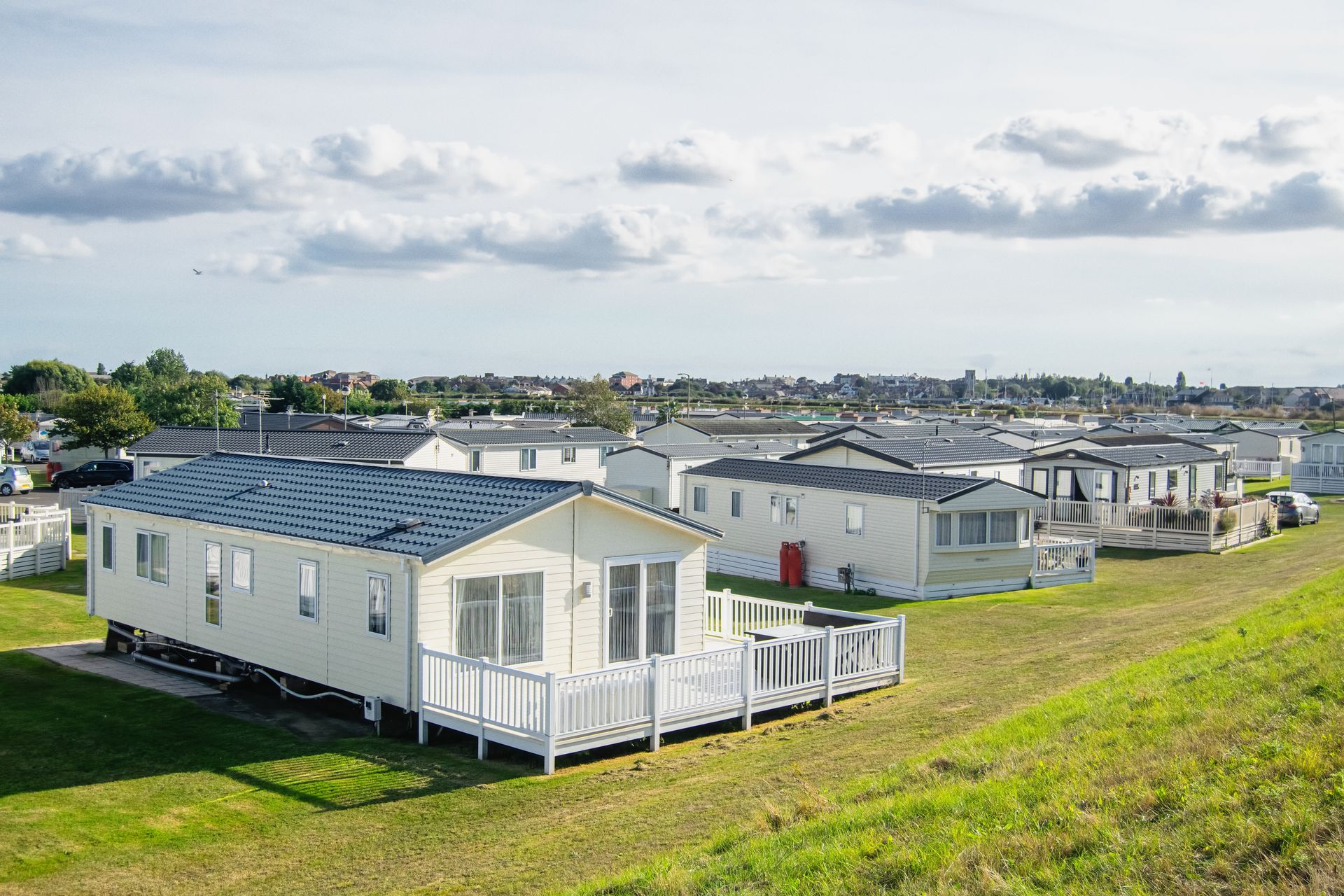 Row of modern mobile homes with decks set on a grassy hillside beneath a bright, cloudy sky.