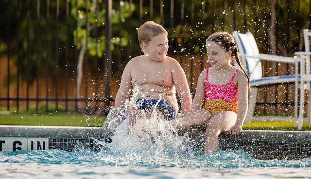 Two children in swimwear splash and laugh in a pool on a sunny day