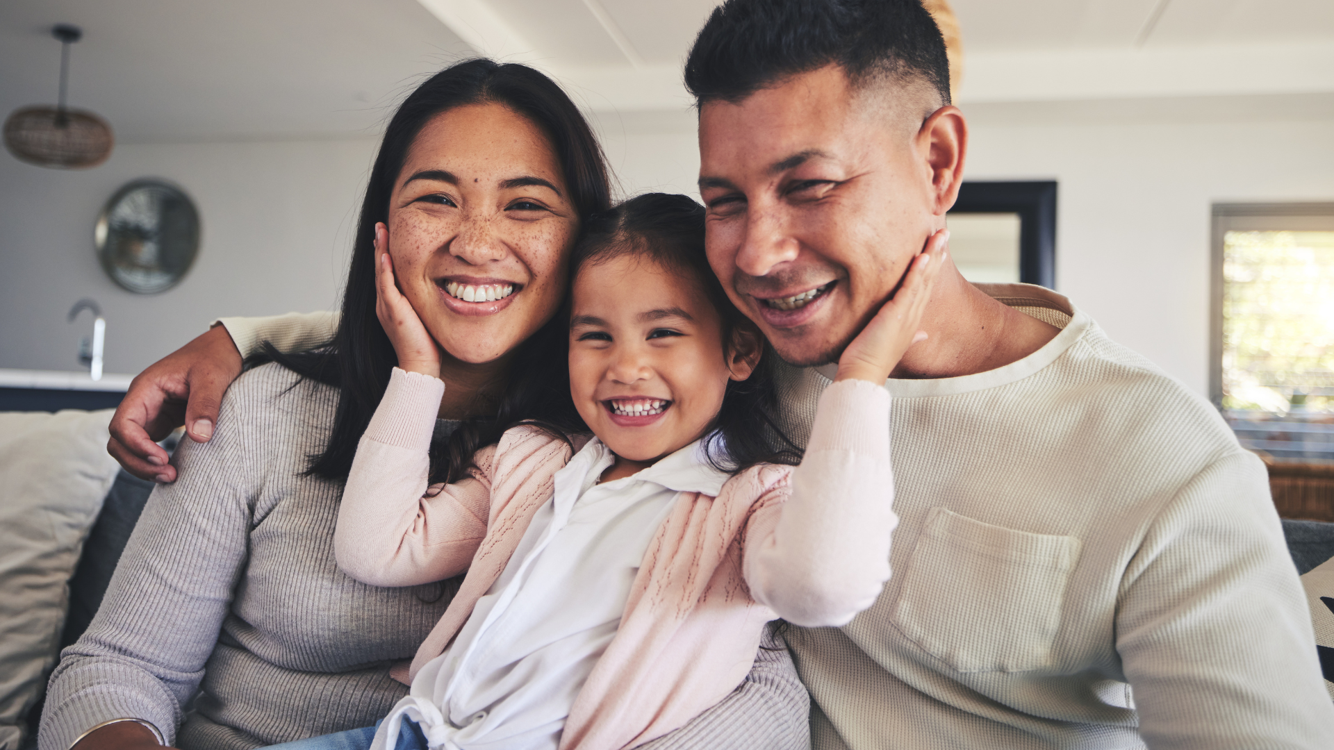 Three people smiling and hugging on a couch in a bright living room
