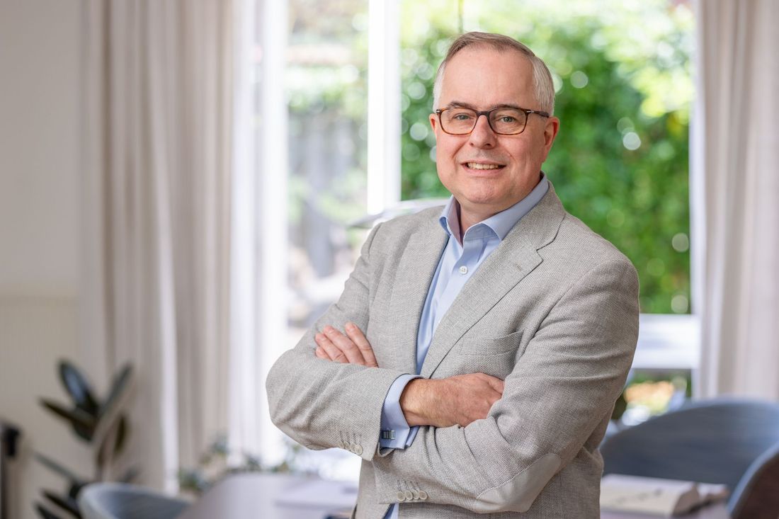 Portret van een lachende man met bril en gekruiste armen in een lichte kantooromgeving.