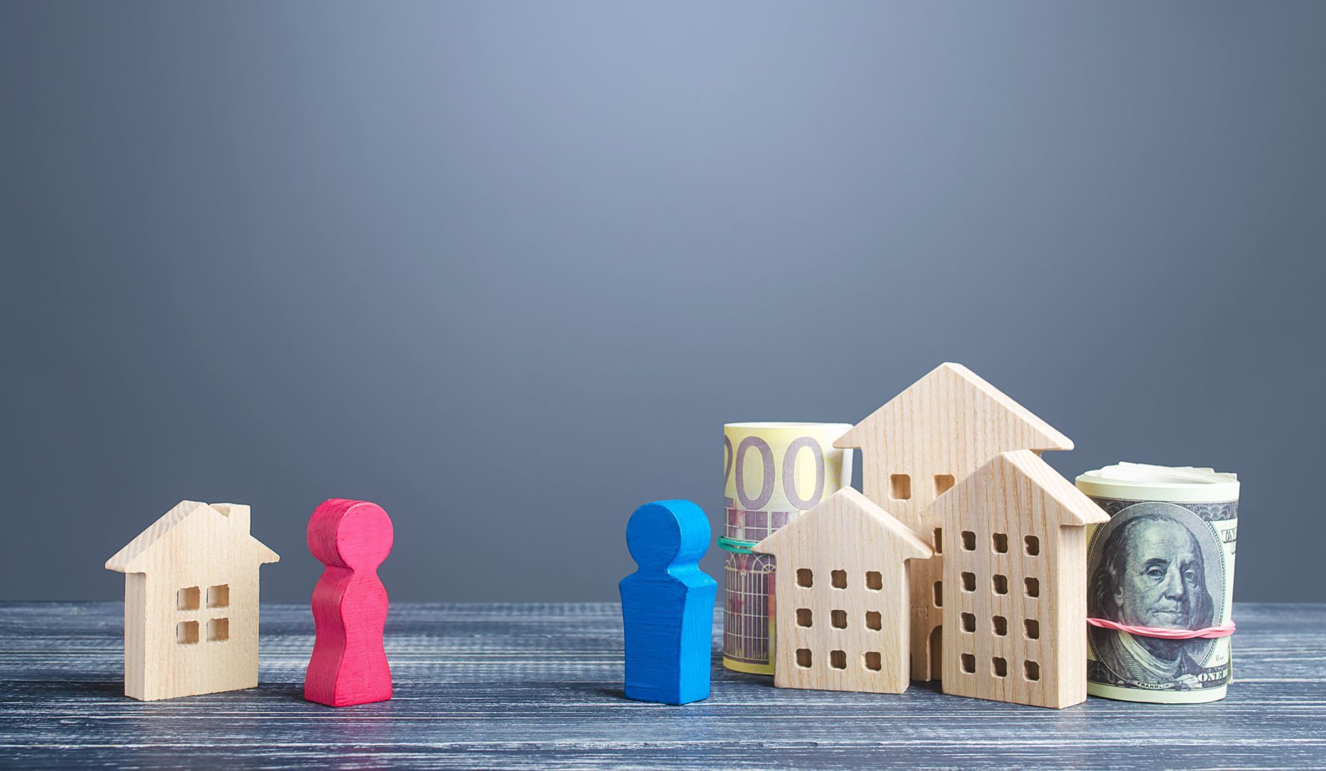 A couple of wooden figures standing next to a bunch of wooden houses and money.