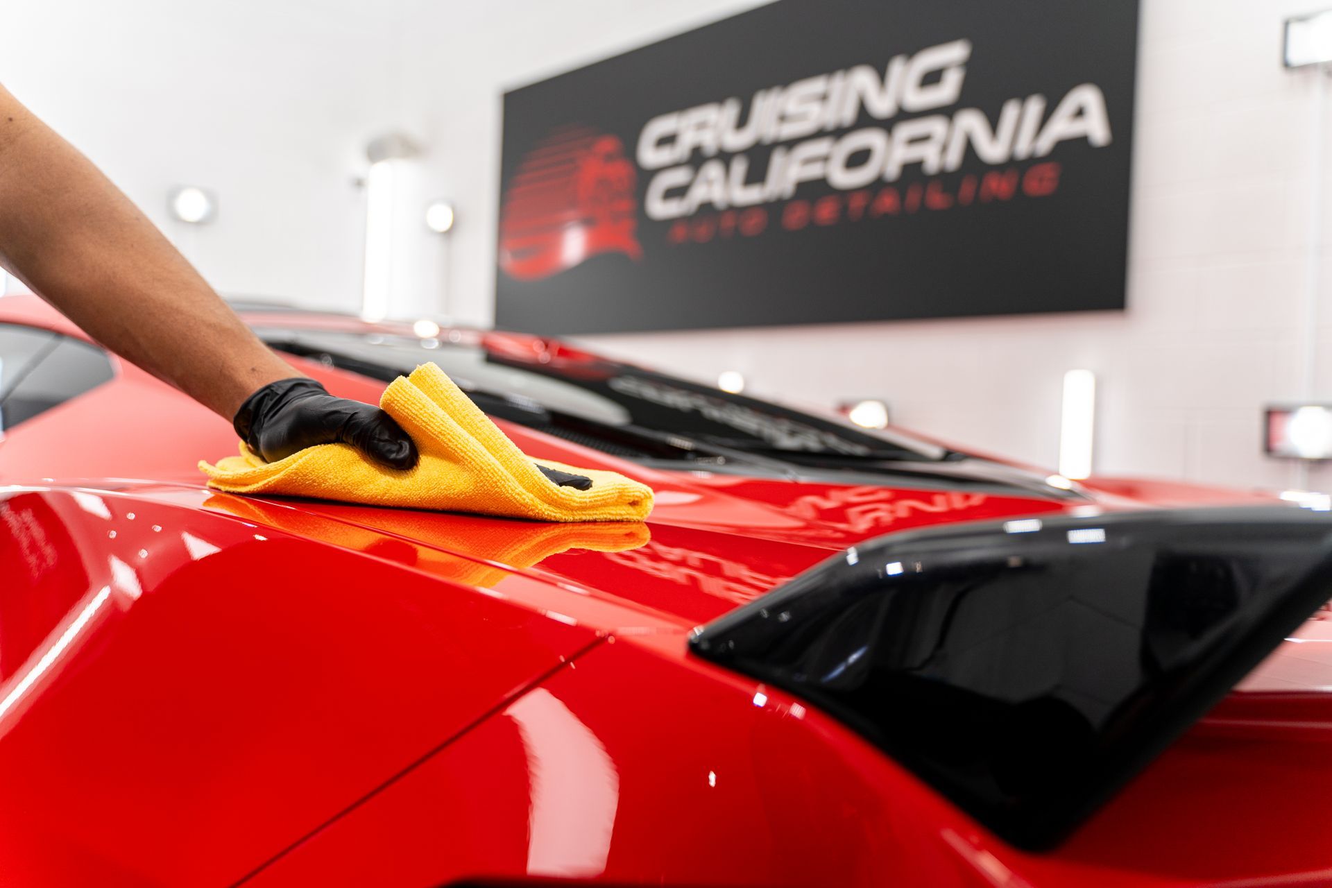 A person is cleaning a red car with a yellow cloth.