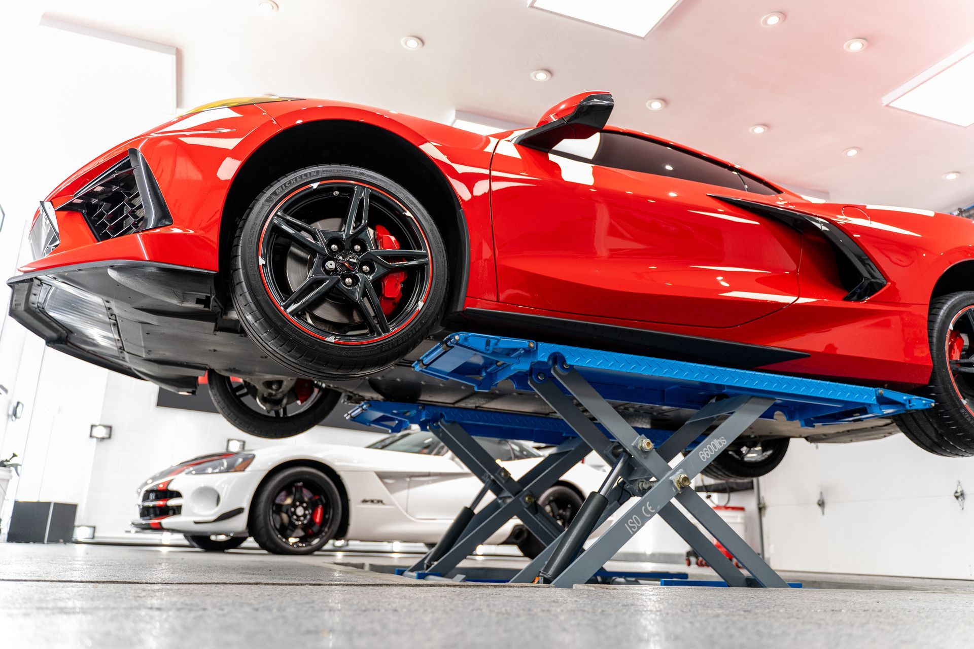 A red corvette is sitting on a lift in a garage.