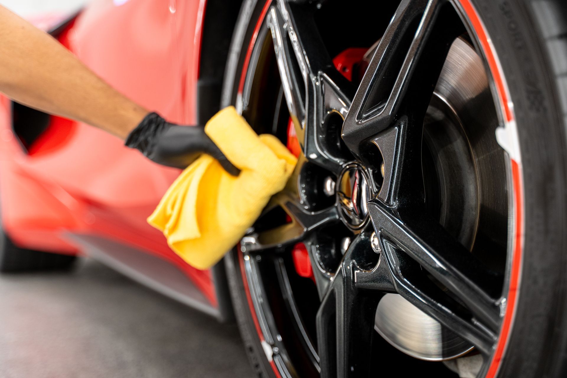 A person is cleaning a car wheel with a yellow cloth.
