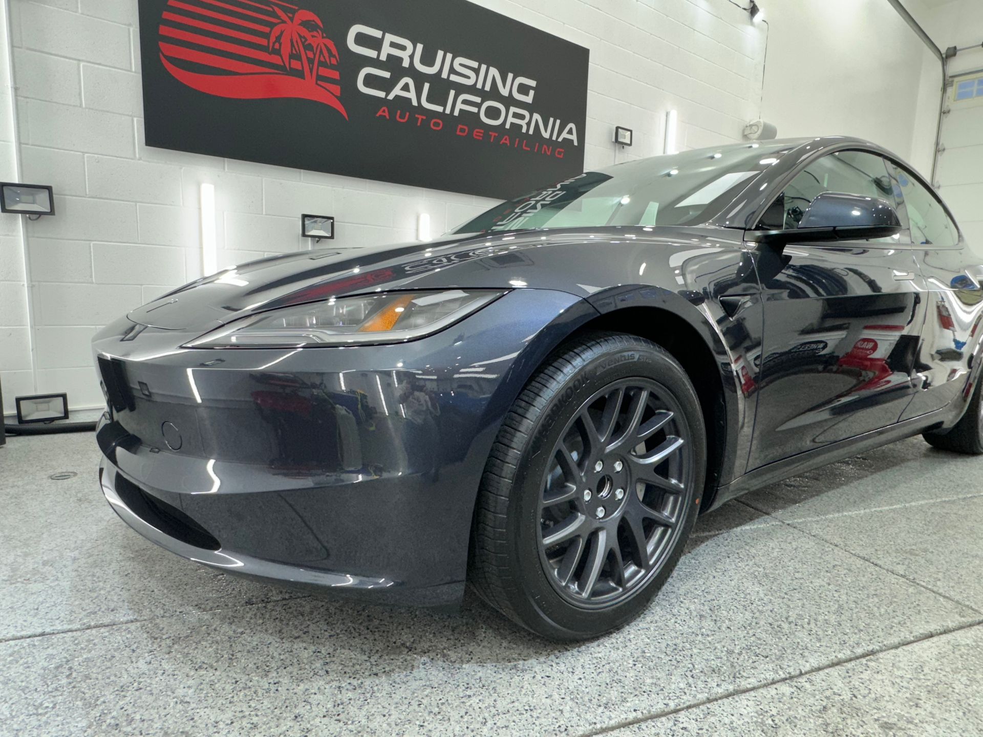A black tesla model 3 is parked in a garage.