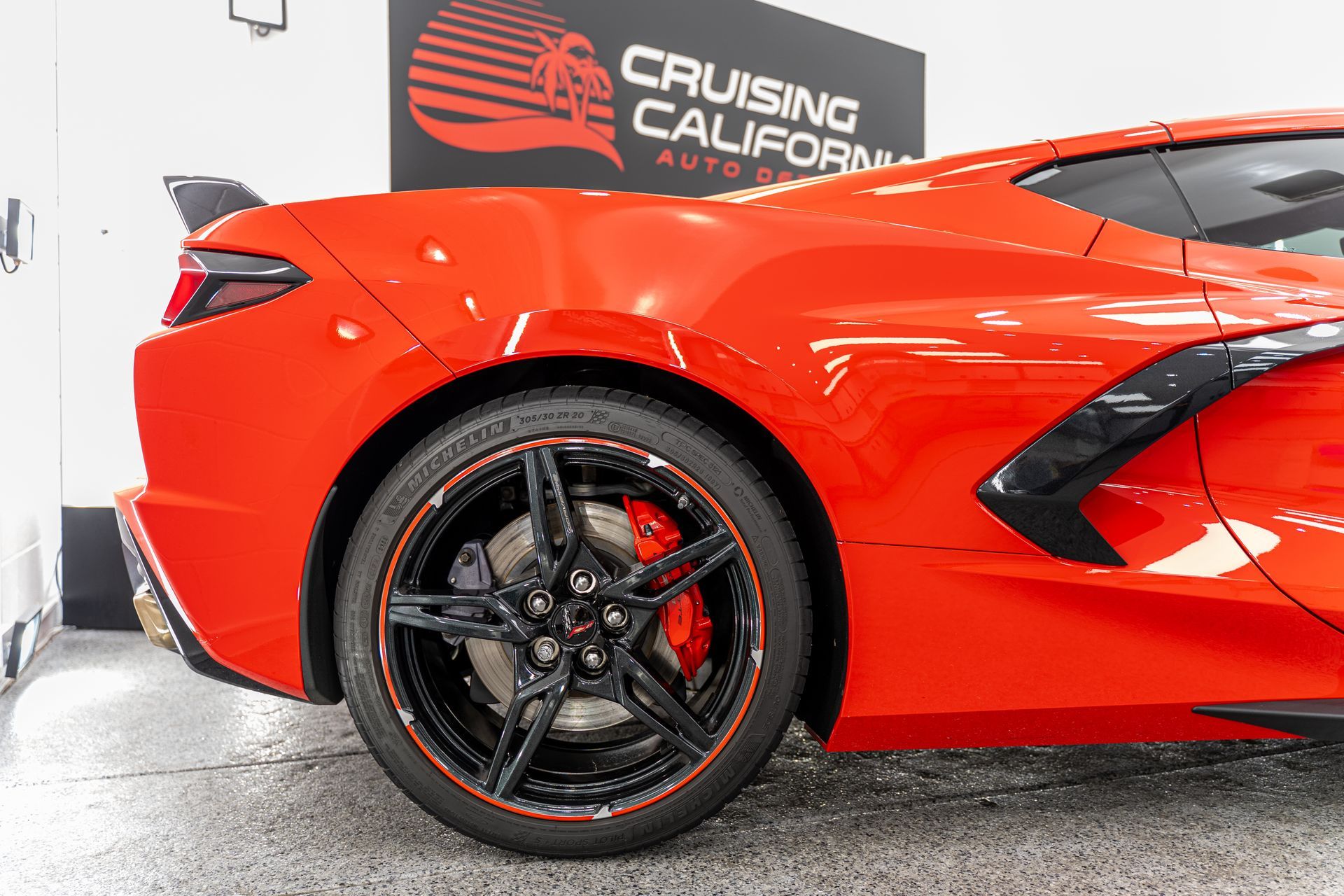 A red sports car is parked in front of a cruising california sign.