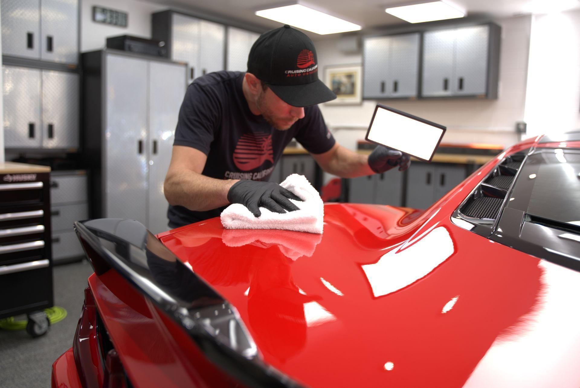 Detailing shop worker polishing a red car with a cloth in a garage