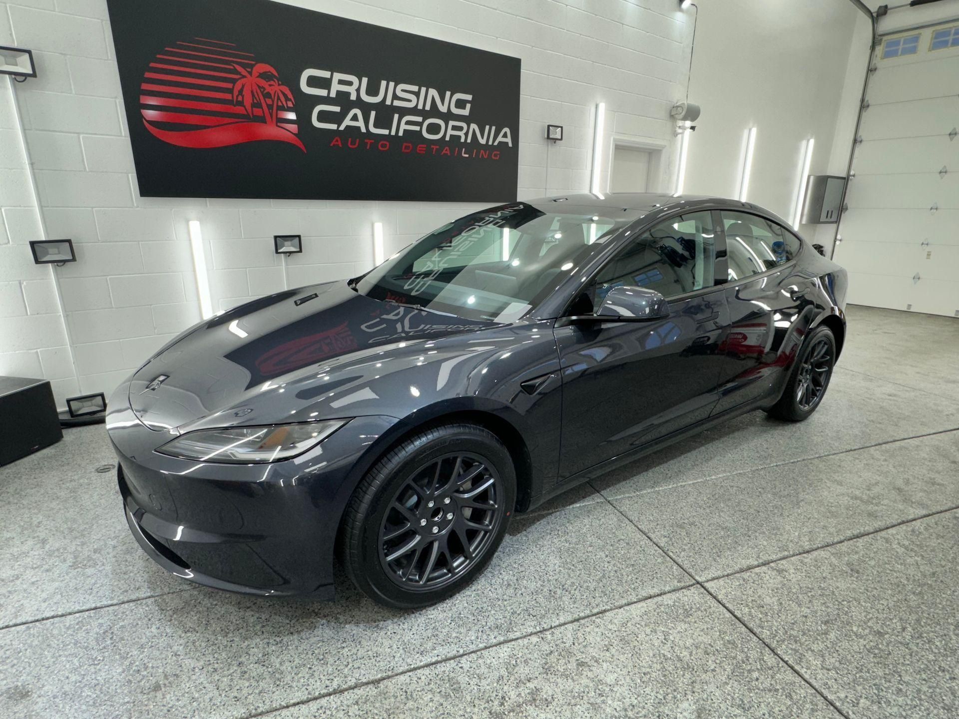 Dark gray Tesla sedan in a showroom with a Cruising California sign on the wall