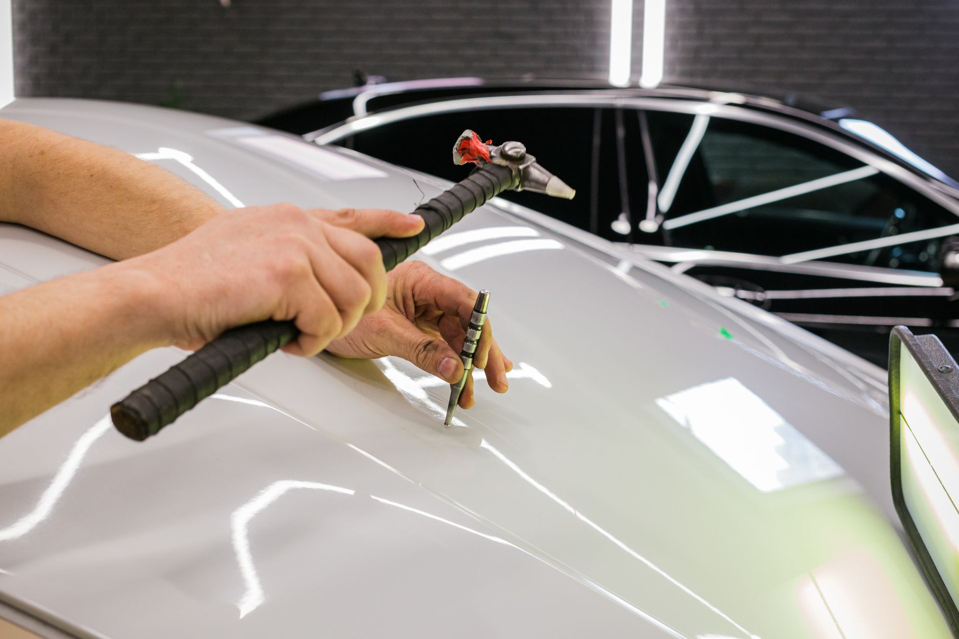 Hands polishing a white car hood with a microfiber cloth and detailing tool