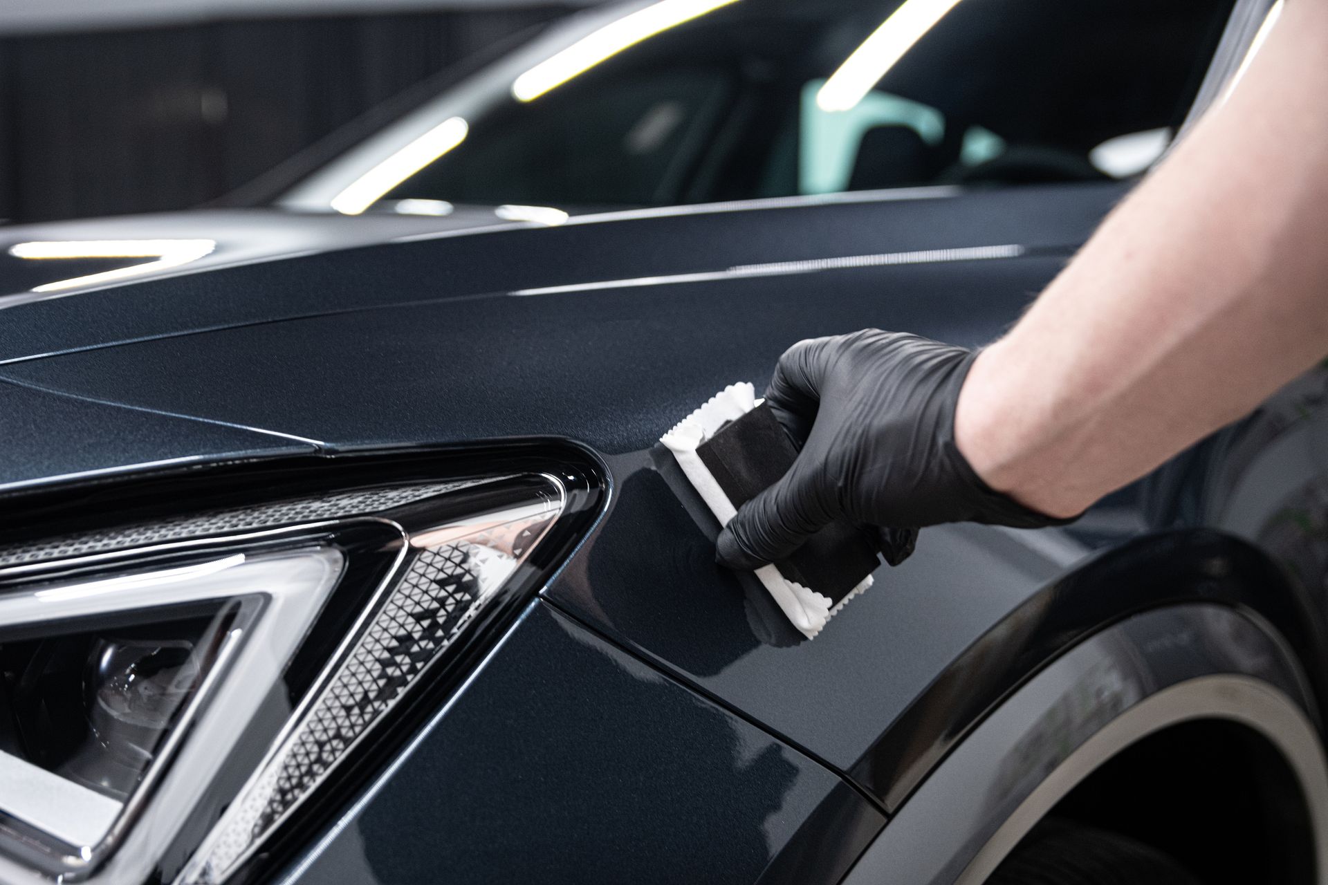 Gloved hand applying film to a black car’s front fender