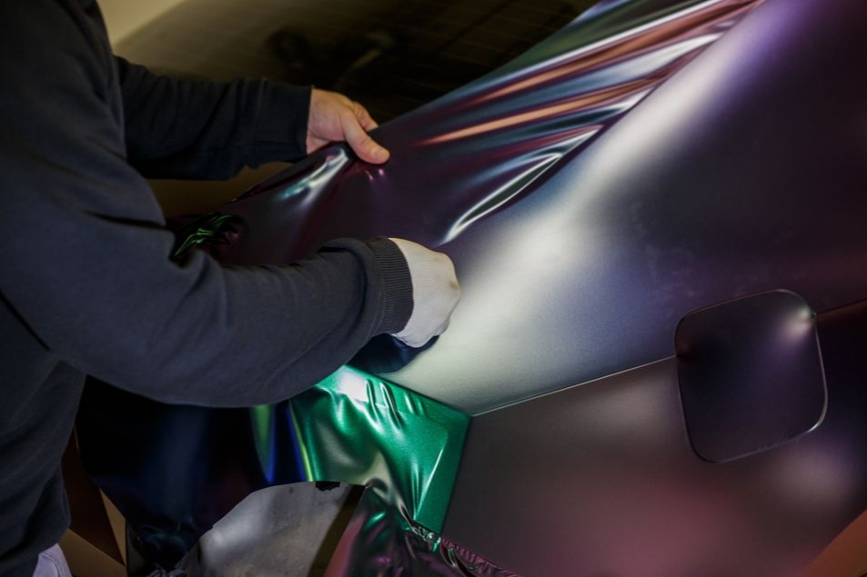 Hands smoothing a glossy purple car wrap in a workshop