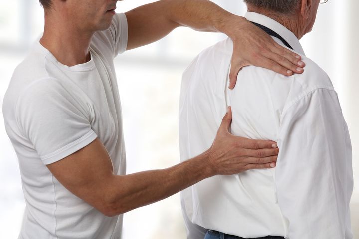 Physical therapist performing back and shoulder assessment on patient for pain relief and rehab care.