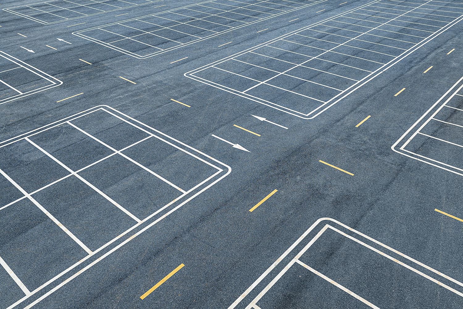 A HIGH-ANGLE VIEW OF AN EMPTY ASPHALT CAR PARK WITH WHITE AND YELLOW ROAD MARKINGS.
