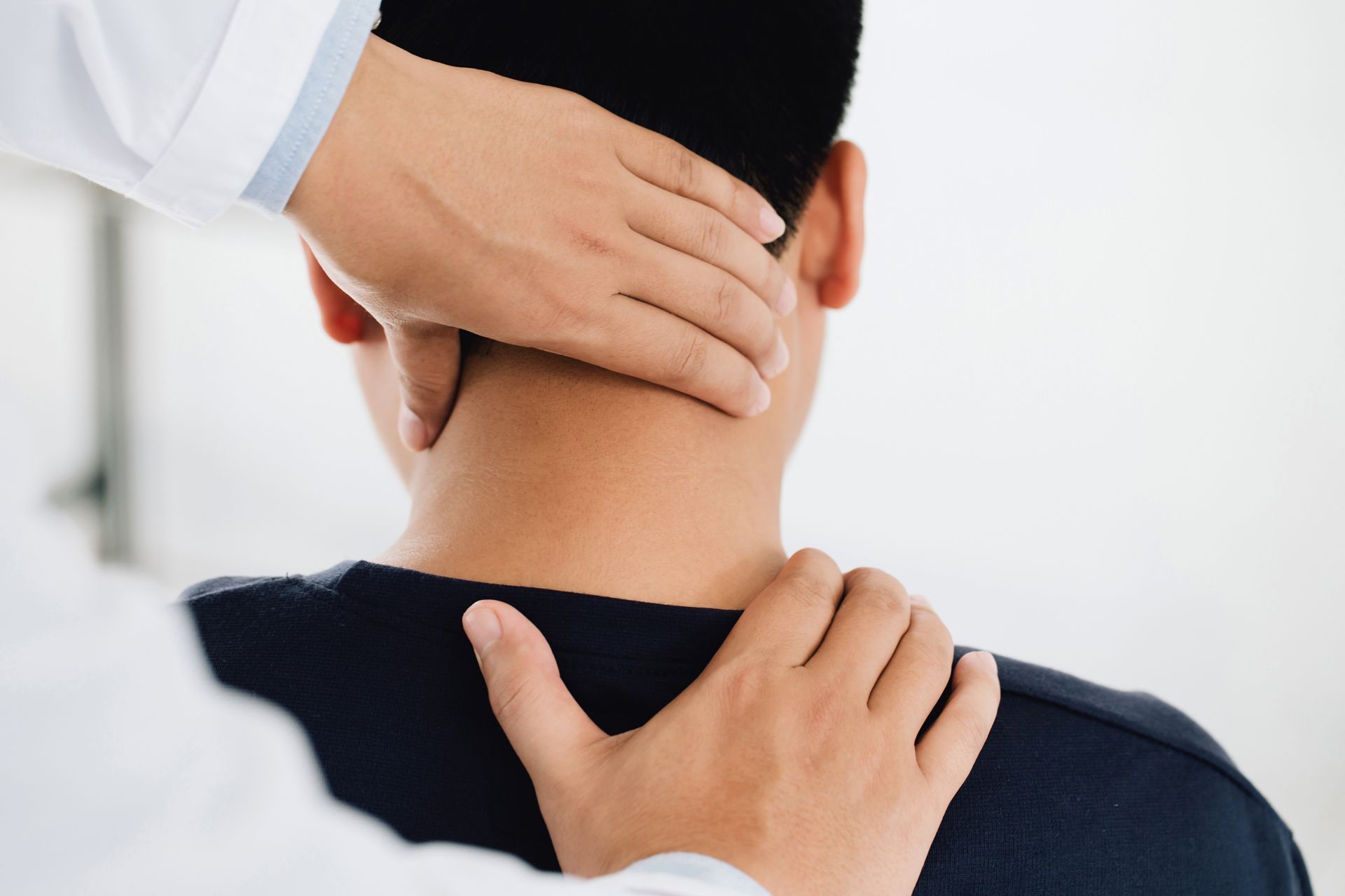 Hands of a person in a white coat are examining the neck of another person.